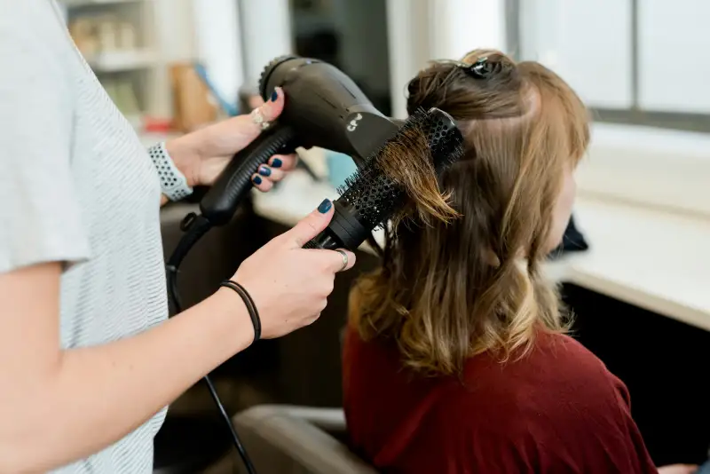 Friseurin föhnt die Haare einer Kundin mit der Rundbürste